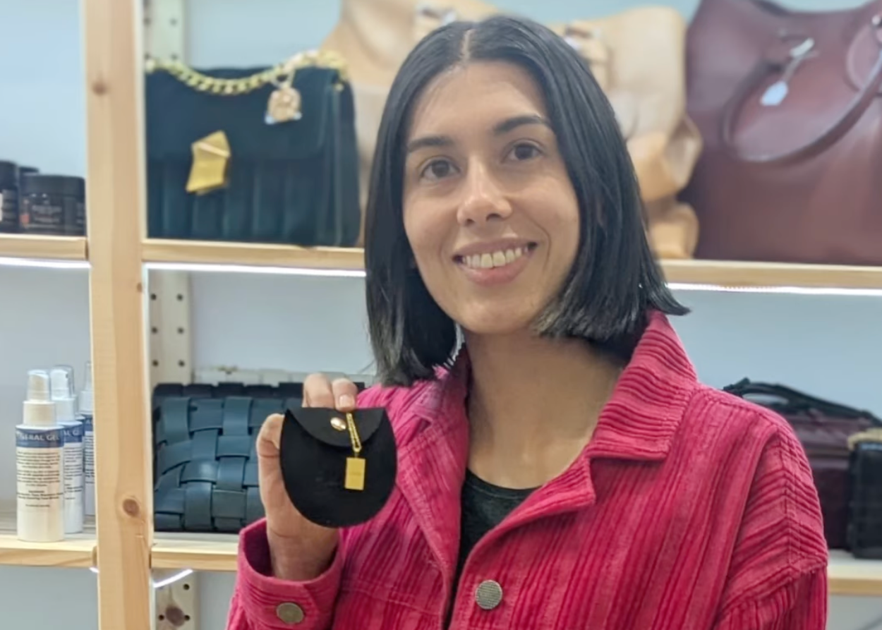 Person wearing a red jacket holding a small object in front of shelves with bags and products.